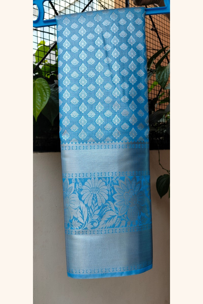 Sky blue brocade saree on hanger showing wide silver tissue border detail